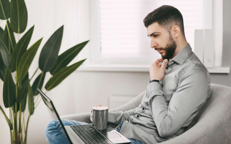 A handsome young man of oriental appearance works at home with a laptop. Doing homework online. Distance learning.